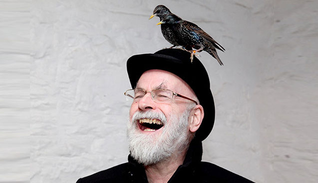 man with gray beard wearing a black jacket glasses and black hat with two black birds sitting on his hat with a white background